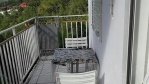 A balcony with a table and chairs, a view of a mountainous landscape, and a white railing.