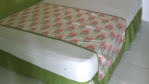 A small, single-bed room with a green wall, patterned curtains, and a green bedspread.