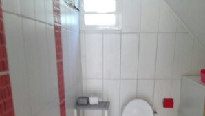 A bathroom with a toilet, a small shelf with toiletries, and a wooden chair.