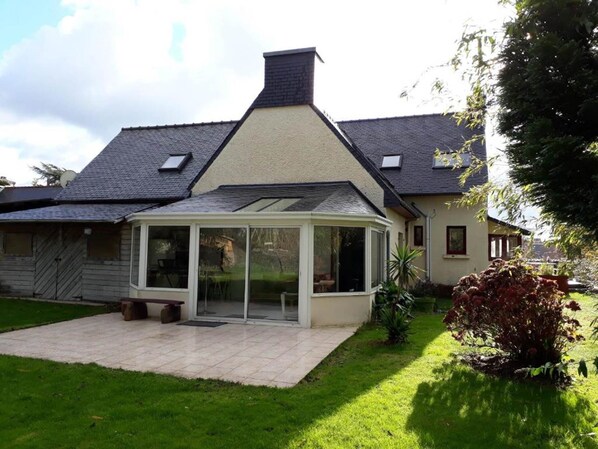 A house with a conservatory, a garden, and a sloped roof.