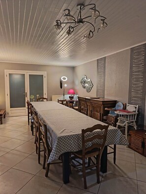 A dining area with a long table, chairs, a chandelier, and a wall-mounted mirror.