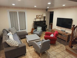 A living room with a sofa, armchairs, a coffee table, a TV, a piano, and a guitar.