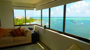 A room with a large window overlooking the sea, a sofa, and a suitcase.