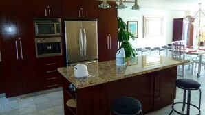 A modern kitchen with dark wood cabinets, stainless steel appliances, a granite countertop, and a bar area with stools.