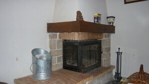 A fireplace with a stone surround, a metal bucket, and a wicker chair. - Gîte Jaune - House on 5 ha property, swimming pool, sauna, animals, (Osse-En-Aspe)