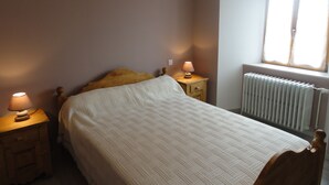 A bedroom with a bed, two bedside tables with lamps, a window with curtains, and a radiator. - House completely renovated character located 1 km from the Gorges du Bès (Arzenc-d'Apcher)