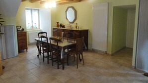 A dining area with a wooden table and chairs, a radiator, and a window with blinds. - House completely renovated character located 1 km from the Gorges du Bès (Arzenc-d'Apcher)