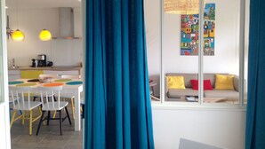 A modern living space with a dining area, kitchen, and a sofa by a window.