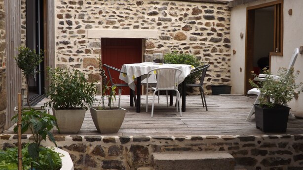 A stone-walled outdoor patio with a table and chairs, surrounded by potted plants.