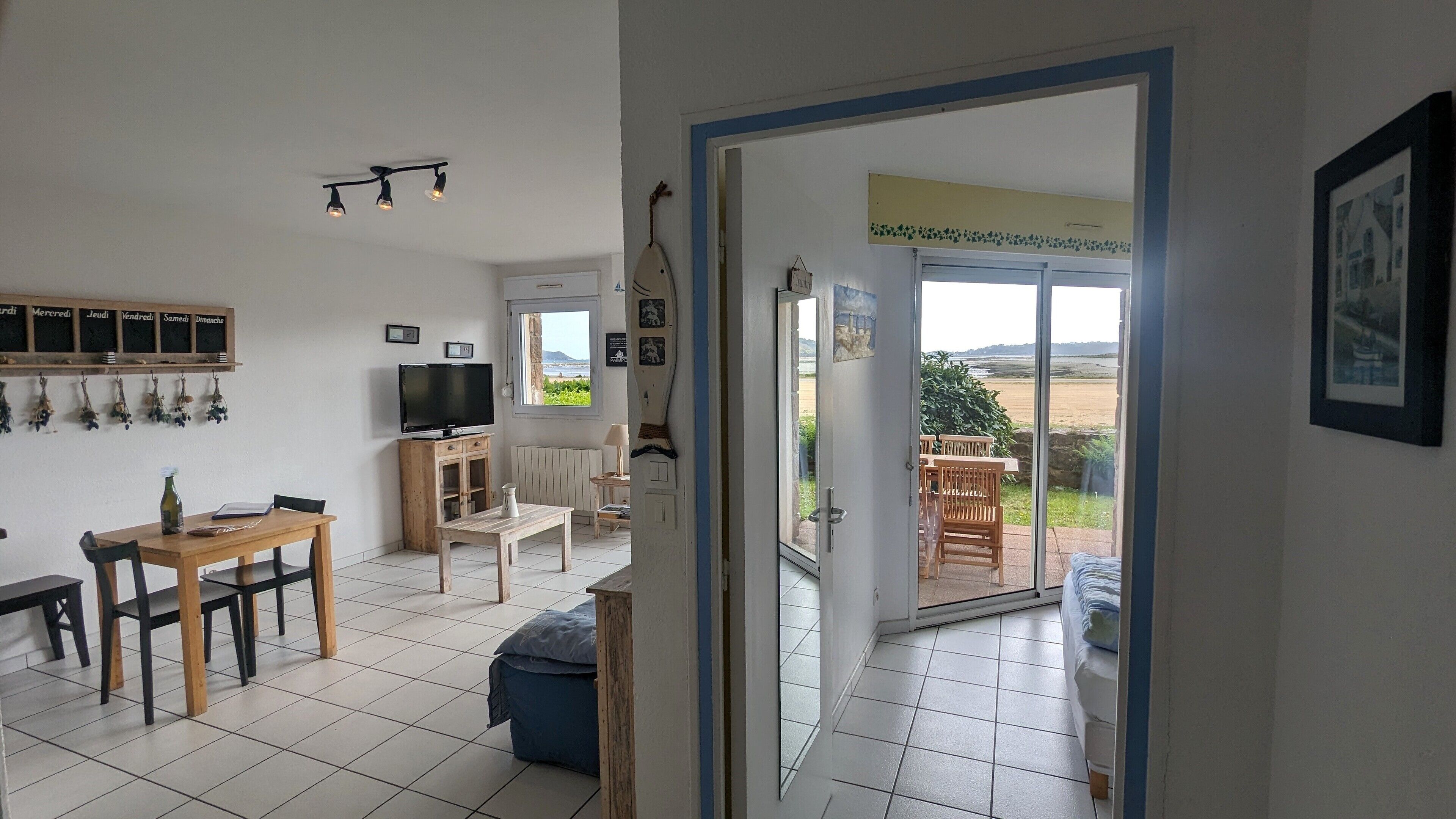A room with a dining table, chairs, a television, and a view of the outdoors through a door.