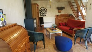 Een gezellige woonkamer met een houten kast, rieten stoelen, een rode bank en een blauwe voetenbank.