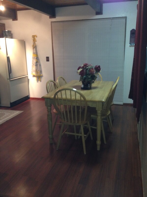 Un comedor con una mesa y sillas de madera, un refrigerador y una puerta con cortina.