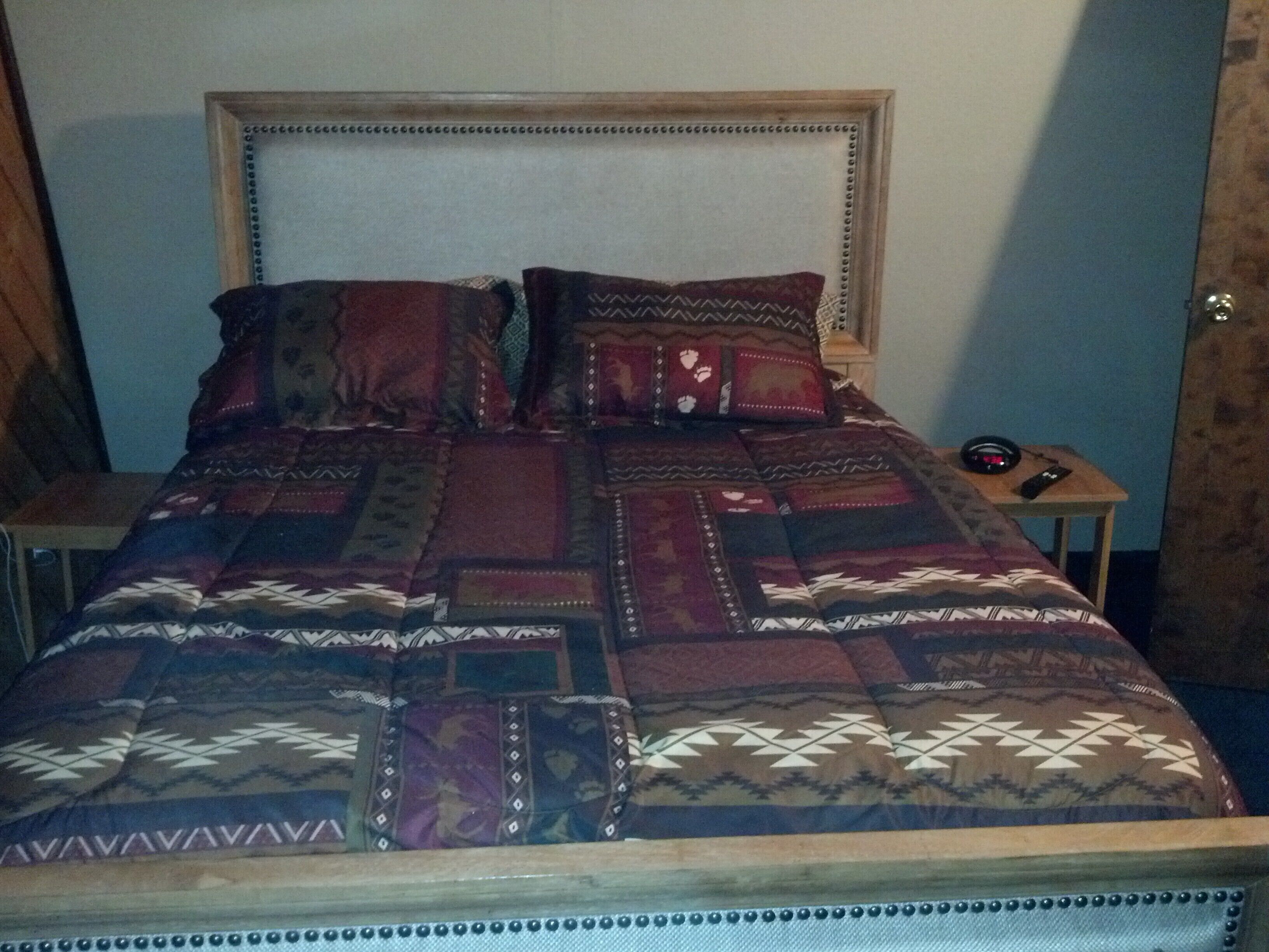 Una cama con colcha estampada, cabecera de madera y mesita de noche con control remoto.