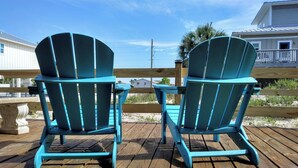Two turquoise Adirondack chairs on a wooden deck with a view of a beach and houses in the background. - A secluded 3 bedroom, 2 bath Gulf view home nestled in lush tropical vegetation (St George Island)