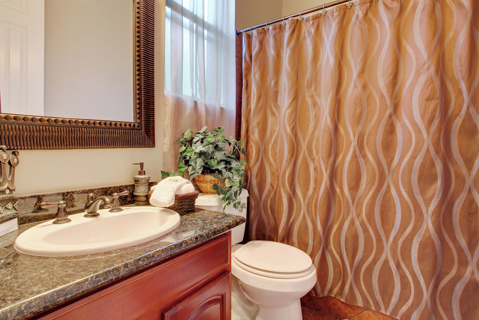 A bathroom with a granite countertop sink, a white toilet, and a shower curtain with a wavy pattern.