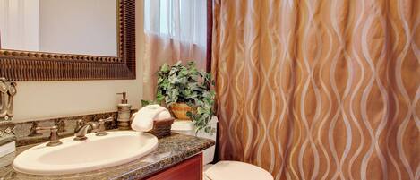 A bathroom with a granite countertop sink, a white toilet, and a shower curtain with a wavy pattern.