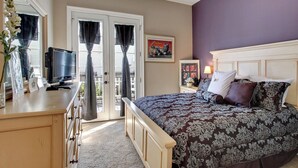 Une chambre à coucher avec un lit, un bureau, une télévision et une fenêtre avec des rideaux.