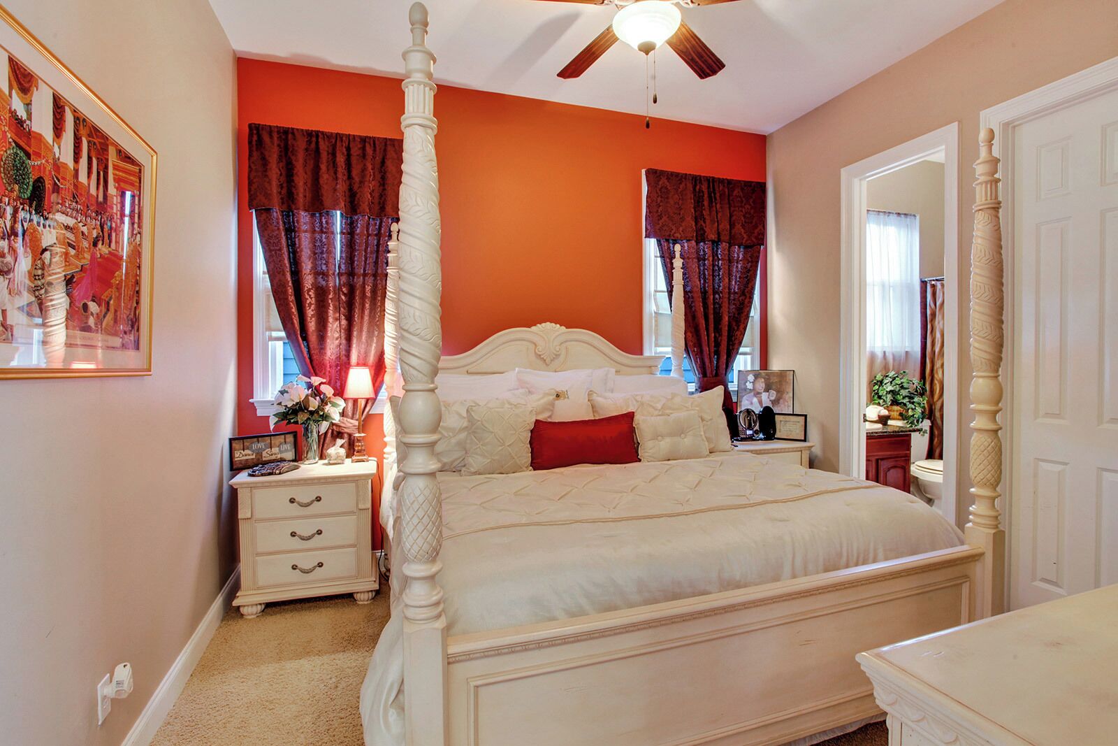 A four-poster bed with a white headboard, a nightstand with a lamp, and a framed picture on the wall.
