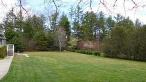 A grassy backyard with a house, trees, and a small garden area. - Beautiful Mountain Getaway - All Four Breathtaking Seasons! (Hendersonville)