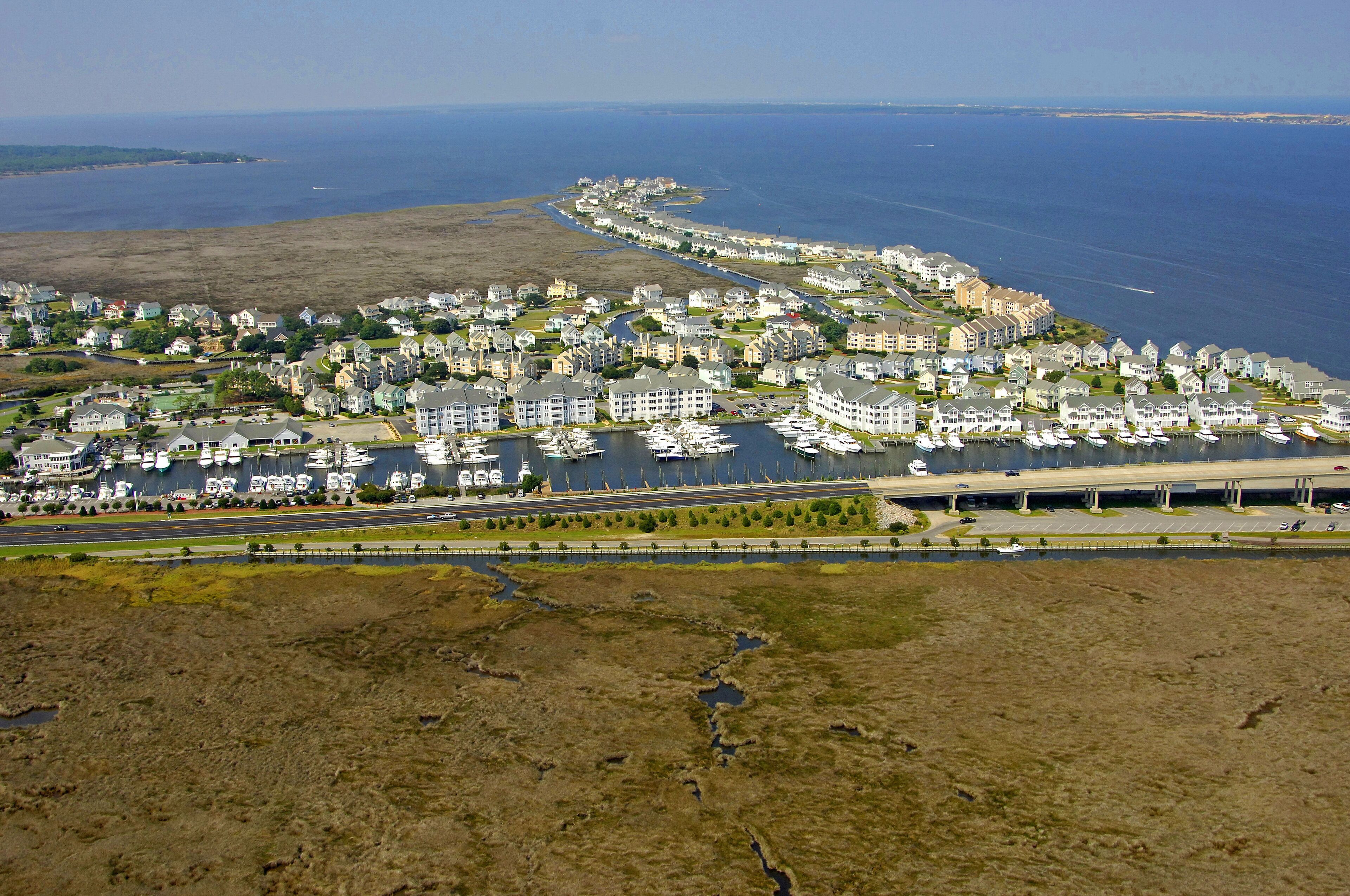 Vista aèria d'una zona residencial costanera amb cases, un port esportiu i una autopista.