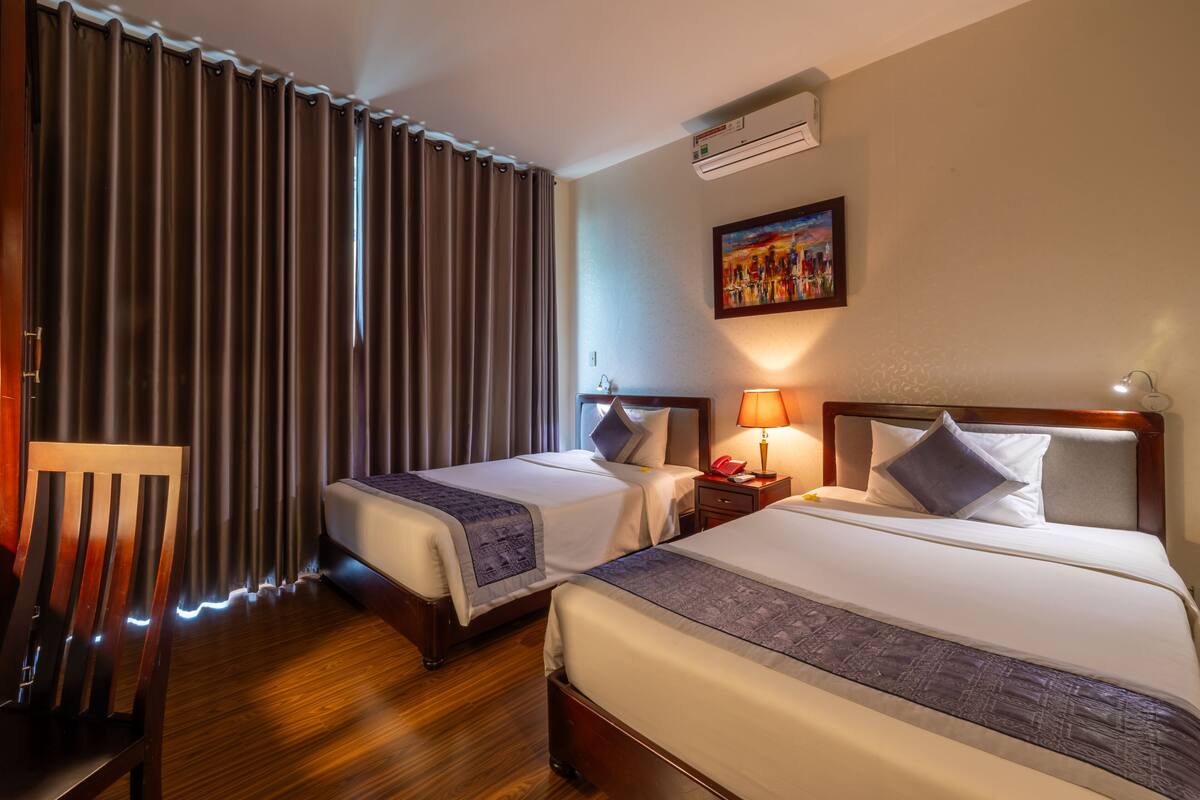A hotel room with two beds, a wooden chair, a nightstand with a lamp, and a painting on the wall.