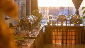 Un buffet proposant une variété de plats, avec une vue sur le paysage urbain grâce à de grandes fenêtres.