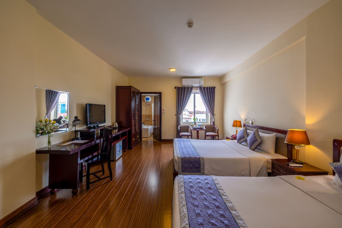 A hotel room with two beds, a desk, a television, and a small seating area with chairs.