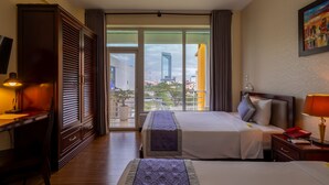 Une chambre d’hôtel avec un grand lit, un bureau, une chaise, une télévision et une vue sur le paysage urbain par les fenêtres.