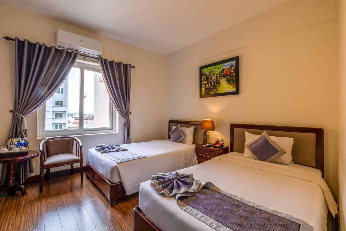 A hotel room with two beds, a chair, a small table with a tray, and a painting on the wall.