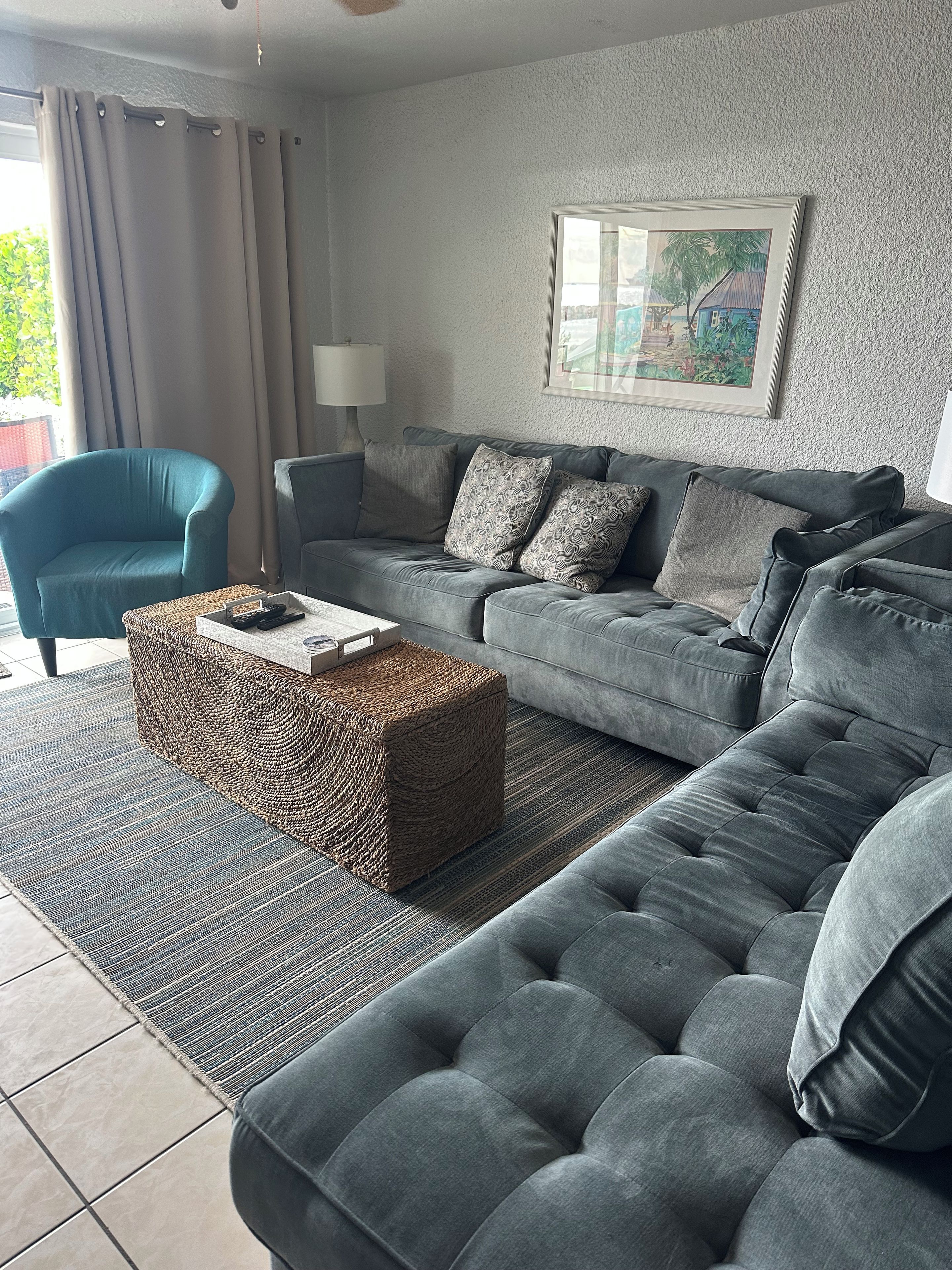 Un salon moderne avec un canapé gris, un fauteuil bleu, un pouf en osier et un tableau encadré accroché au mur.