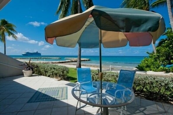 A patio with a table and chairs, a beach view, and a ship in the distance.