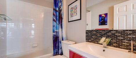 Un baño con inodoro blanco, bañera, cortina de ducha, lavamanos con espejo y pared con azulejos.