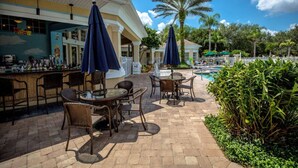 An outdoor bar area with wicker furniture and umbrellas, a pool in the background, and palm trees. - Windsor Palm Resort/Pool /3 miles to Disney (Kissimmee)