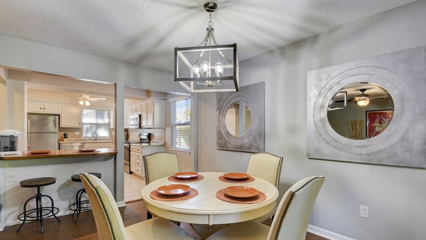 A dining area with a round table, four chairs, and a chandelier. There is a kitchen in the background with a refrigerator and cabinets. - ♥Cozy Townhome w Lux Beds♥Full Kitchen♥ Deck♥Park access two doors down♥ (Overland Park)
