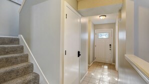 A hallway with a carpeted staircase, a white door, and a tiled floor. - ♥Cozy Townhome w Lux Beds♥Full Kitchen♥ Deck♥Park access two doors down♥ (Overland Park)