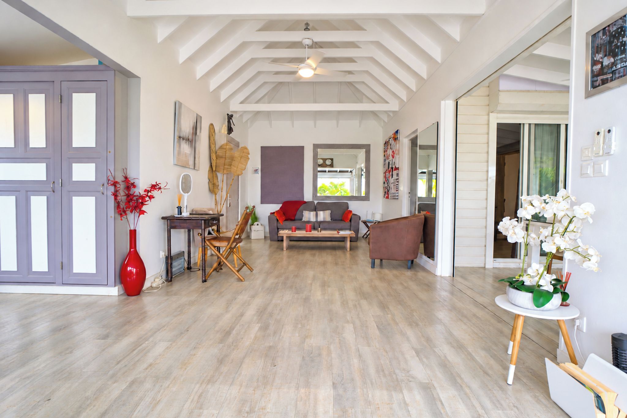 A spacious living room with a high ceiling, a sofa set, a coffee table, and a red vase with red flowers.