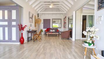A spacious living room with a high ceiling, a sofa set, a coffee table, and a red vase with red flowers.