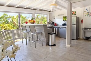 A modern kitchen with a bar area, a dining set, and a view of tropical vegetation. - Guest-House In A Palmgrove For A Couple. Space, Privacy And Silence (Saint Martin)