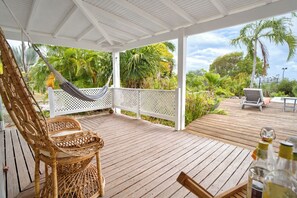 Eine Holzterrasse mit einer weißen Pergola, einem Korbstuhl, einer Hängematte und einem Tisch mit Flaschen.