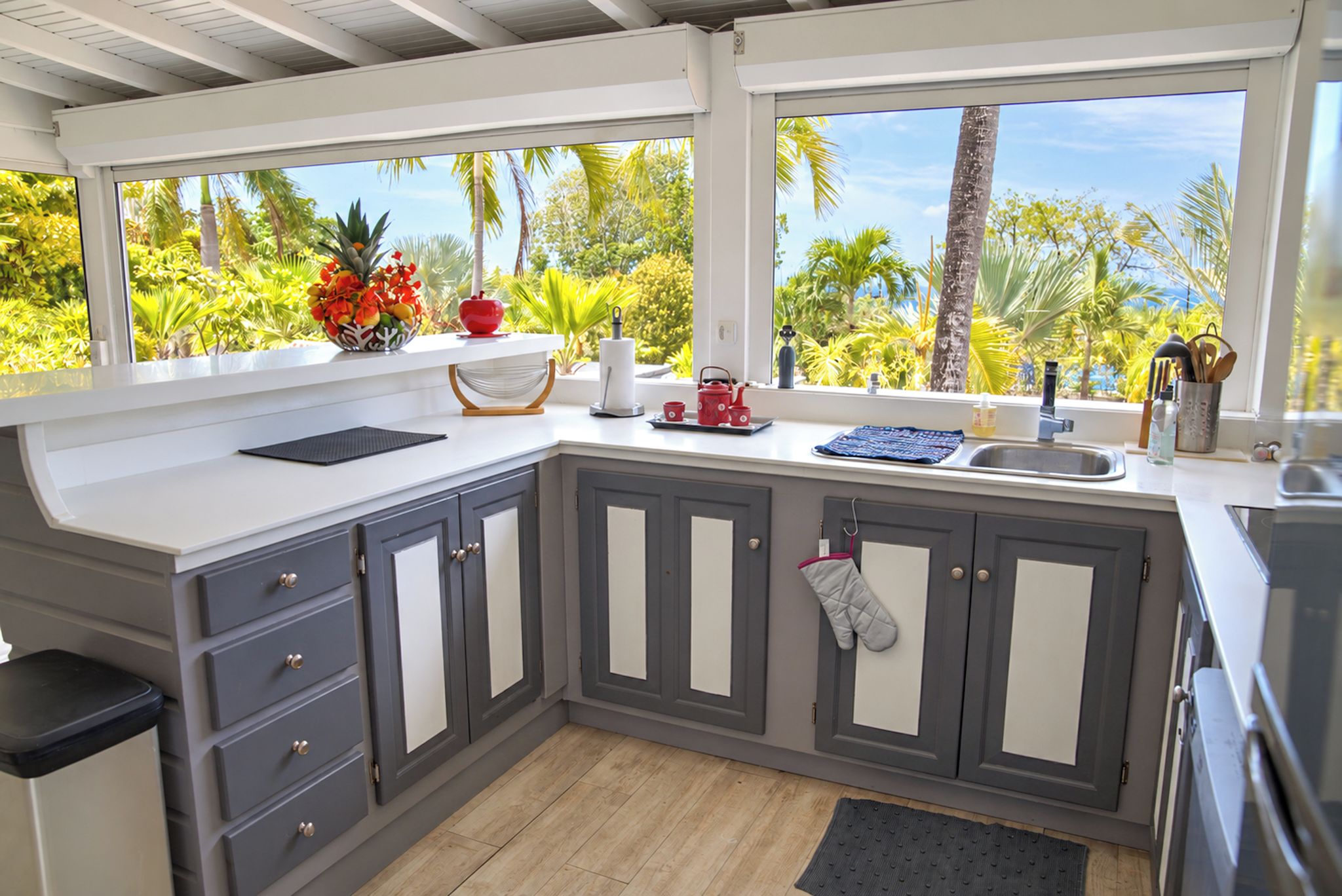 A kitchen with grey cabinets, a white countertop, and a view of palm trees.