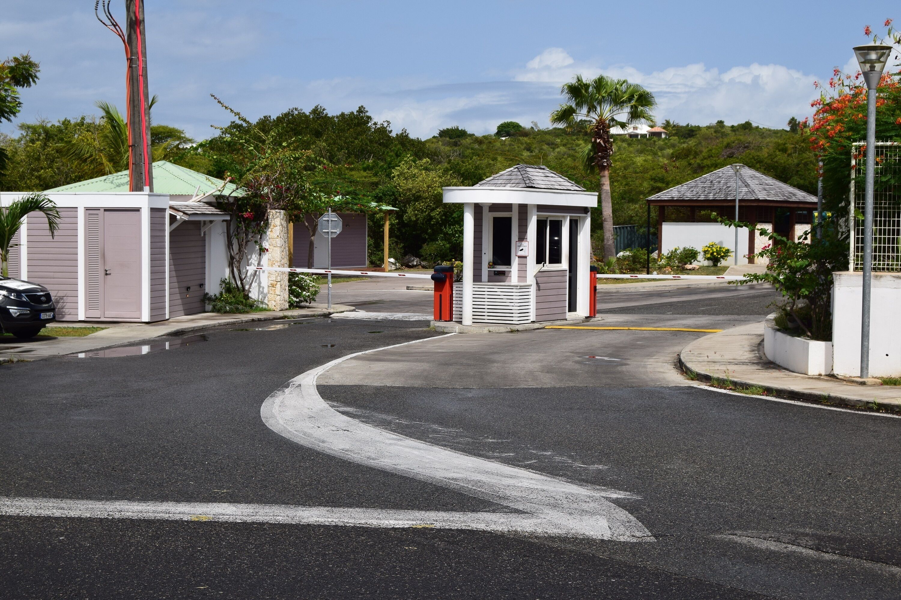 A gated residential area with a small gazebo, a covered outdoor seating area, and a street with a curved road.