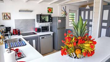 A kitchen with a stainless steel refrigerator, a microwave, and a toaster. There is a sink with a faucet and a dish rack. A vase with red flowers and fruits is on the counter.