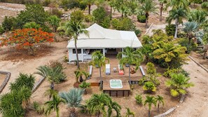 Une maison dotée d’une grande terrasse, entourée de diverses plantes tropicales et comprenant un jacuzzi.