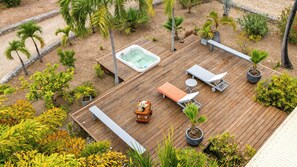 Una terraza de madera con jacuzzi, sillas de descanso y plantas en macetas.
