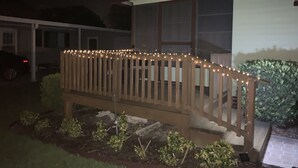 Eine Holzbank mit Lichterkette, ein weißes Haus und ein Garten.