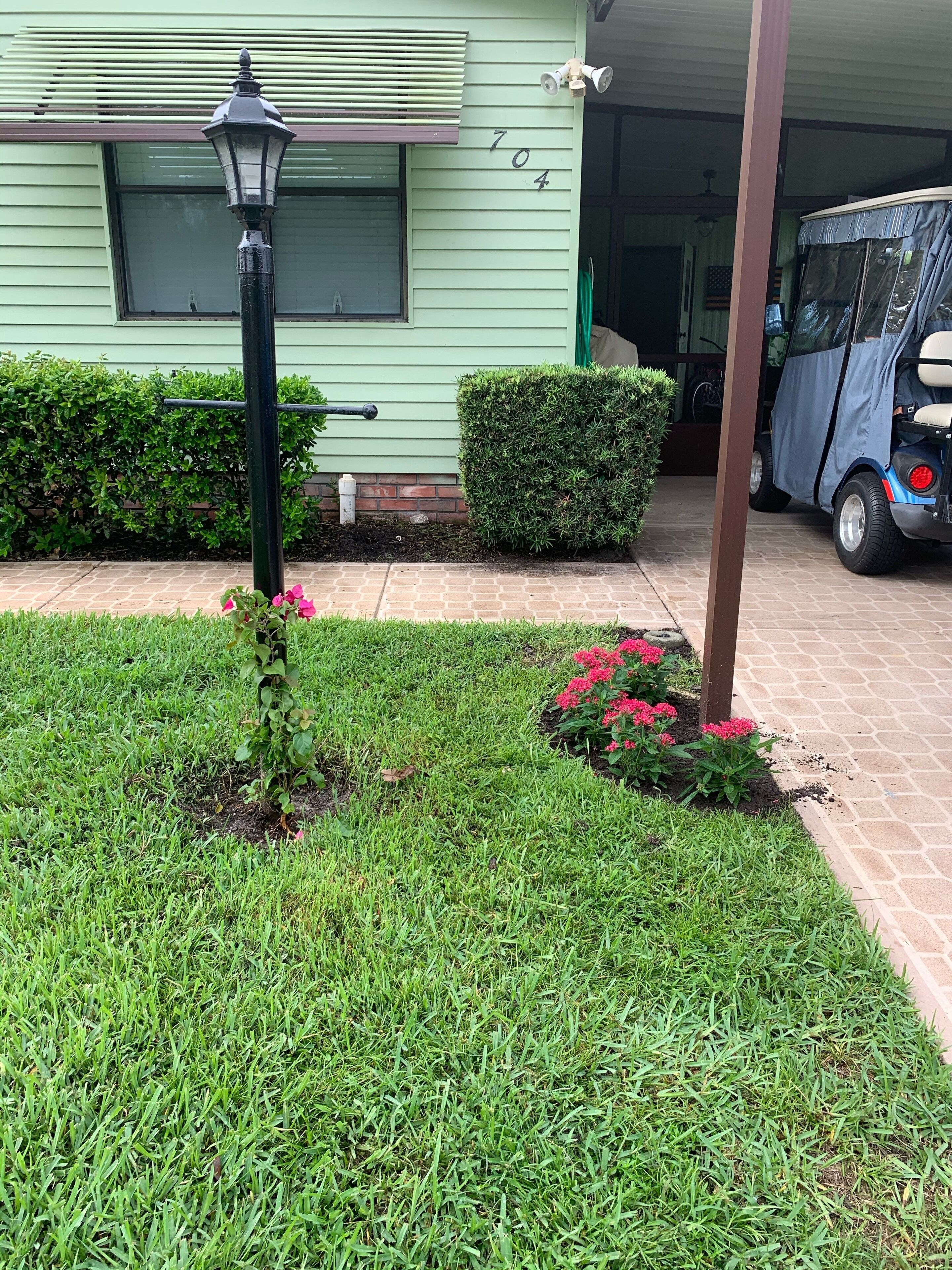 A green house with the number 704, a lawn with pink flowers, and a parked three-wheeled vehicle.