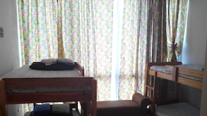 A dormitory room with bunk beds, a small table, and a window with floral curtains. - Affordable Condo with FREE WIFI and Amenities (Cebu City)