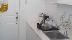 A small kitchen with a white door, a sink, and a countertop with a dish rack and a few kitchen items. - Affordable Condo with FREE WIFI and Amenities (Cebu City)