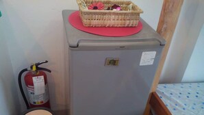 A compact room with a grey refrigerator, a small wooden bed with a blue and white patterned bedspread, a red mat on the refrigerator, and a fire extinguisher beside it. - Affordable Condo with FREE WIFI and Amenities (Cebu City)