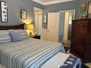 Une chambre à coucher comprenant un lit, une table de chevet, une commode et une porte donnant sur une autre pièce.